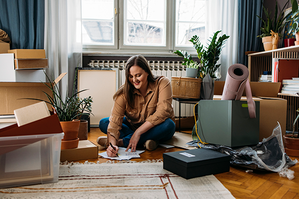 A woman sitting between moving boxes on the floor of a living room 